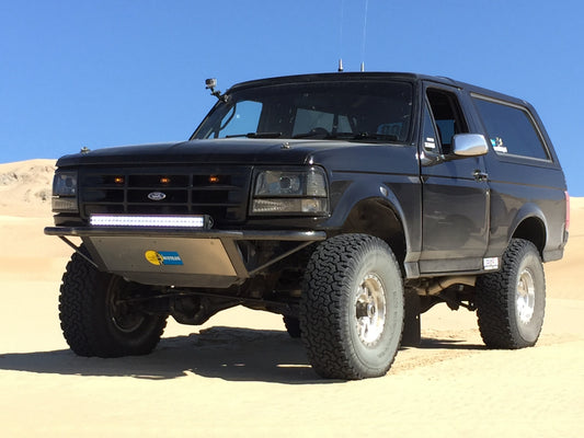 A '92 - '96 Ford Bronco with a LED retrofit kit installed on it, parked on a sandy surface with a clear blue sky in the background.