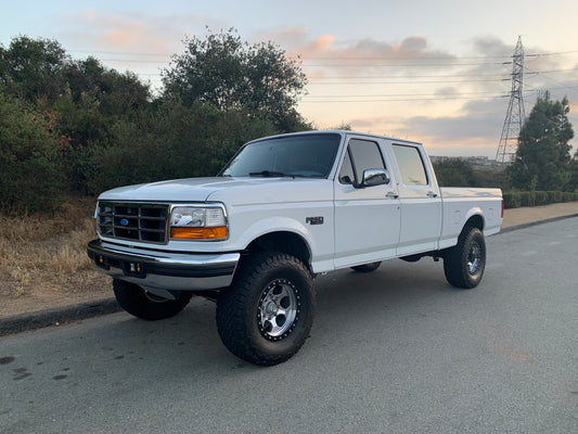 White pickup truck on a road with trees and power lines in the background
