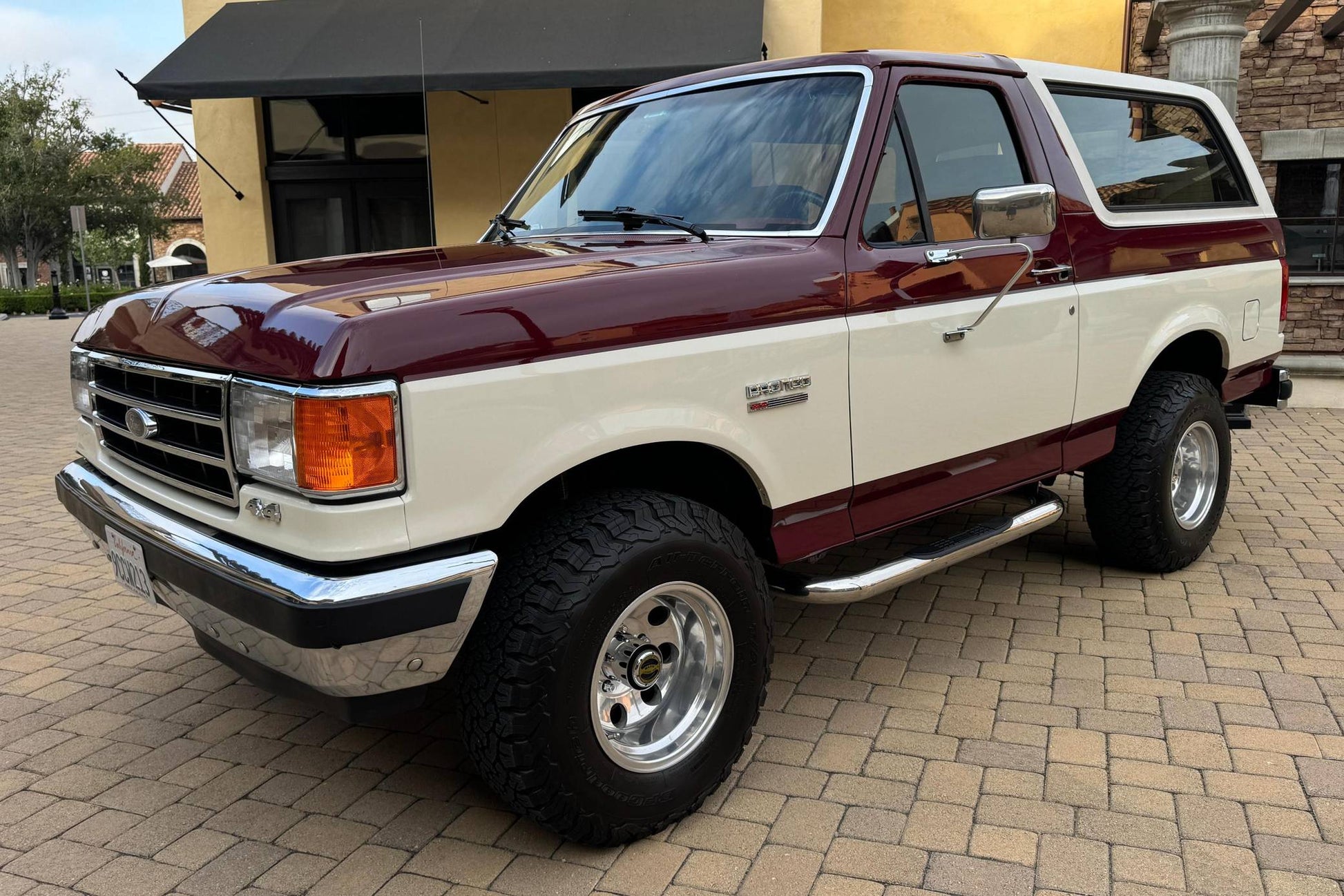 Vintage Ford Bronco SUV with maroon and beige exterior parked on a brick driveway.