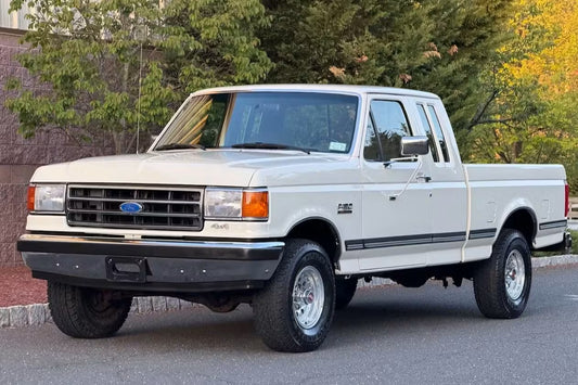 White pickup truck parked on a street with trees in the background