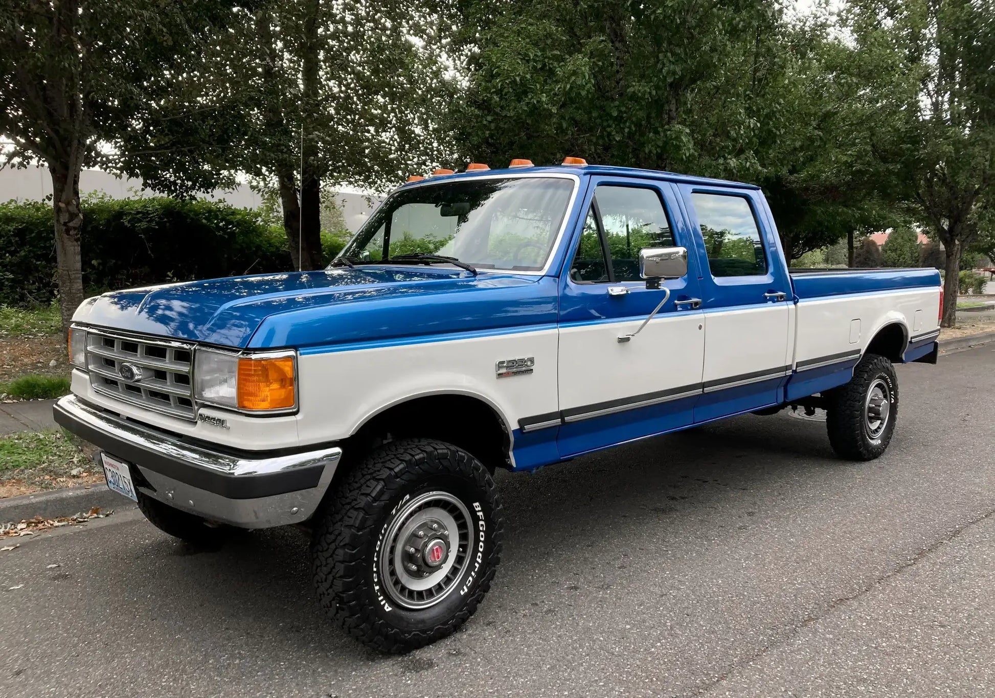 Blue and white pickup truck parked on a street with trees in the background